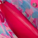 Cartera shopper de símil cuero con diseño multicolor en tonos fucsia, celeste y blanco. Tiene acceso abierto, un bolsillo interno con cierre, asas fijas y herrajes plateados.