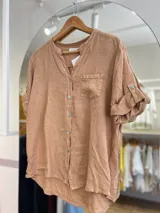 Camisa color marrón claro de lino, con cuello mao, manga corta con trabilla y bolsillo de parche en el pecho.