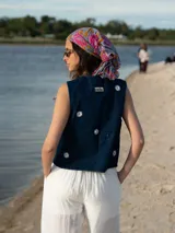 Chaleco de denim azul con bordado de margaritas blancas y logo de la marca en la parte superior.