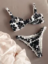Conjunto de bikini blanco con estampado de hojas negras. El corpiño es de corte recto con breteles anchos y nudo central. La bombacha es vedetina con nudos en los laterales.