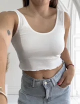 Musculosa ajustada de tejido acanalado (morley), con escote redondo y bordes ondulados en el ruedo. Disponible en colores beige, blanco y negro.