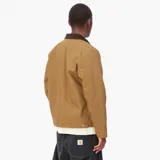 Chaqueta de estilo workwear en color tostado, con cuello de pana en contraste marrón oscuro. Cuenta con cierre frontal de cremallera, un bolsillo con cierre en el pecho y el parche con el logo de la marca en el frente.