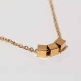 Collar dorado con cadena de eslabones y tres dijes cúbicos.