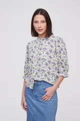 Blusa estampada con flores azules y hojas verdes, cuello mao con volados, mangas 3/4 con volados en los puños y cierre frontal con botones.