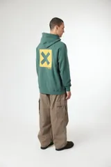 Hoodie azul marino con capucha, bolsillo canguro y cordones ajustables. Presenta un pequeño parche cuadrado amarillo con una 'X' y texto en japonés en el pecho.