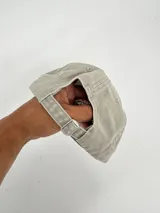 Gorro tipo gorra de béisbol, color gris claro con visera azul. Presenta un bordado frontal con el texto "Soft Rock Cafe" y un diseño de un globo terráqueo con detalles en rojo, azul y verde.