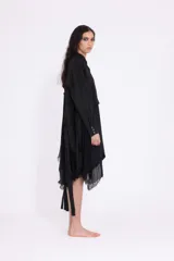 Vestido camisero negro de largo midi, con diseño asimétrico y efecto de capas. Presenta cuello clásico, cierre frontal de botones y mangas largas con puño. El bajo es irregular y deshilachado.