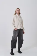 Campera de poliéster tipo sherpa en color natural, con diseño holgado, cuello alto y cierre frontal completo. Presenta un bolsillo de parche con cierre en el pecho y mangas largas con puños elásticos.