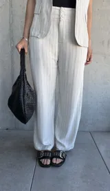 Pantalón de vestir color natural con finas rayas verticales negras, de corte holgado y tiro alto.