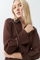 Camisa de vestir marrón con cuello clásico, cierre frontal con botones, mangas largas con puños abotonados y detalles de pespuntes blancos en cuello, solapa y canesú.