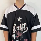 Remera negra de estilo futbol americano con mangas cortas, cuello en V con ribete doble en blanco y bordó, y estampado frontal con la palabra "Drift" y otros diseños gráficos en blanco y rojo.