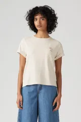 Remera color crudo de corte recto, con cuello redondo y mangas cortas con dobladillo. Tiene un bolsillo en el pecho con bordado de una flor.