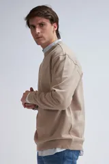 Sudadera de tejido liso color beige, con cuello redondo y puños y ruedo acanalados. Se lleva superpuesta a una camisa de cuadros celestes y blancos.