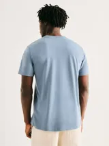 Camiseta blanca de algodón con cuello redondo y mangas cortas. Estampa rectangular con borde negro que contiene la frase "NATURAL ATMOSPHERE" en letras mayúsculas y una imagen de montañas y mar.