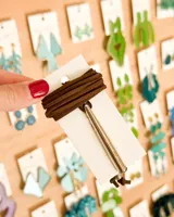 Choker de tiento marrón enrollado, con dije colgante metálico alargado de color plateado.