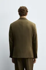 Blazer color verde oliva de corte regular, confeccionada en tejido con lana. Presenta cuello con solapas de pico, manga larga con puños abotonados, bolsillo de vivo en pecho, bolsillos de doble vivo en cadera, bolsillo interior y aberturas en la espalda. Cierre frontal cruzado con doble botonadura.