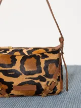 Mini cartera bandolera de cuero con estampado animal print, correa regulable de cuero y pelo, y hebillas metálicas.