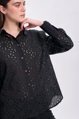 Camisa negra de manga larga con cuello clásico y cierre con botones. Presenta bordado tipo broderie con calados circulares. Corte recto.