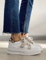 Zapatillas deportivas urbanas con capellada negra, detalles en beige y suela blanca.