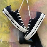 Zapatillas Converse Chuck 70 Ox de lona negra con detalles en blanco, cordones blancos y suela de goma blanca con doble línea negra.