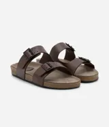 Sandalias slide marrones de cuero sintético con dos tiras ajustables con hebillas metálicas negras y plantilla anatómica.