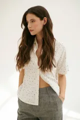 Camisa blanca con estampado de lunares negros, de corte clásico, manga corta y cuello camisero.