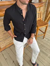 Camisa negra de corte slim, con cuello mao, manga larga con puños abotonados y cierre frontal con botones de madera.