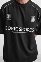 Camiseta negra de corte boxy fit, cuello redondo y manga corta. Presenta logos estampados en blanco en el frente y detalles en verde en los laterales.