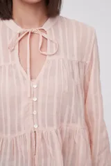 Blusa blanca con rayas verticales, cuello con lazo, mangas largas y corte holgado.