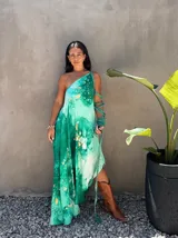 Vestido largo de tela fluida, color verde esmeralda con estampado abstracto en tonos turquesa y detalles dorados. Diseño asimétrico con un solo tirante tejido en el hombro.
