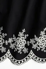 Top negro de algodón con breteles finos que se atan en moño y detalle de bordado floral blanco en el ruedo.