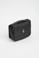 Necesser de viaje negro con cierre de cremallera y asa de transporte. Tiene un parche rectangular con el logo de un avión y la palabra "TRAVEL".