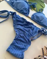 Bikini de dos piezas color azul, con corpiño triangular con volados y tirantes finos ajustables. La bombacha es de corte regulable con lazos laterales y tiene un pequeño frunce en la parte trasera.