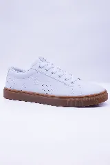 Zapatilla urbana de caña baja, color blanco, con cordones blancos y suela de goma color caramelo. Presenta microperforaciones en el lateral y el logo de un pingüino bordado.