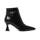 Bota corta de cuero sintético negro con punta fina y taco de aguja. Presenta doble tira fina con detalle de apliques metálicos y dije circular con logo de la marca alrededor del tobillo.
