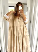 Vestido camisero largo color beige con rayas verticales blancas, cuello camisero, abotonadura frontal y mangas 3/4 con puños blancos.