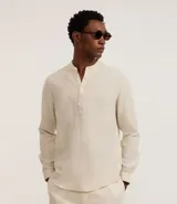 Camisa blanca de manga larga, corte amplio y cuello padre (mandarín). Presenta un frente abotonado con tapeta corta.