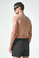 Traje de baño negro con estampado de palmeras blancas, con elástico y cordón en la cintura, bolsillos laterales y trasero con cierre autoadherente.