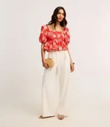 Pantalón wide leg color blanco, confeccionado en crepé, con trabillas en la cintura, cierre tradicional, pliegues y cinturón de cadenas doradas.