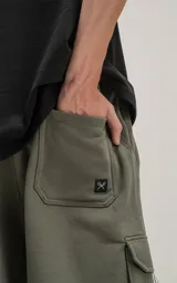 Bermuda de algodón rústico color verde militar, calce oversize, con elástico en la cintura y bolsillos cargo con cierre.