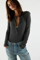 Camiseta tipo henley de manga larga, color blanco, confeccionada en algodón elástico con cuello redondo y tapeta de botones.