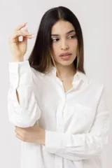 Camisa blanca de lino, de corte holgado, con cuello clásico, cierre frontal con botones, bolsillo en el pecho y mangas largas con puños abotonados.