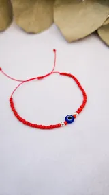 Pulsera roja ajustable con canutillos, separadores plateados y dije de ojo turco.