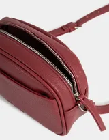 Bandolera negra de cuerina con bolsillo frontal con tag de metal, correa regulable, cierre superior y tirador de material principal.