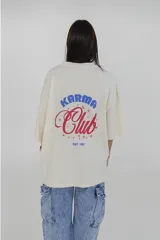 Remera gris de corte oversize con cuello redondo y estampado pequeño en el pecho con la frase "Karma Club" en color lila.