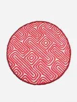 Pareo circular de algodón con estampado geométrico en tonos rojo, rosa y blanco, con flecos en el borde.