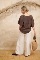 Blusa de lino color beige, con detalles de punto escama en escote y mangas, y prendedor de flor en el hombro. Talle único.