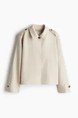 Chaqueta corta color beige, de corte oversized, con cuello clásico, charreteras abotonadas, bolsillos laterales y trabilla con botón en los puños.