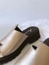 Sandalias doradas con tira para el dedo y suela track negra.