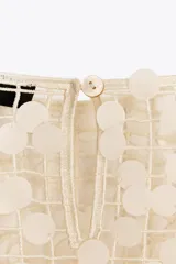 Vestido largo color crema con lentejuelas, de cuello redondo y manga larga. Tiene aberturas laterales en el bajo y cierre con abertura y botón en la espalda.